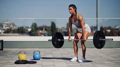 Junge, trainierte Frau macht Rudern mit Kurzhanteln Junge, trainierte Frau macht Rudern mit Kurzhanteln