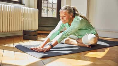 Eine ältere Frau macht eine Dehnübung auf der Yogamatte