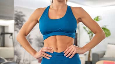 Eine trainierte Frau in blauer Sportkleidung zeigt ihre trainierten Bauchmuskeln