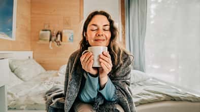 Serene woman savoring the aroma of coffee in her cozy bedroom