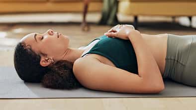 Frau liegt entspannt mit geschlossenen Augen auf einer Yogamatte