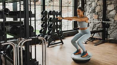 Concentrated woman doing squats on balance board with effort. Interval training in gym.