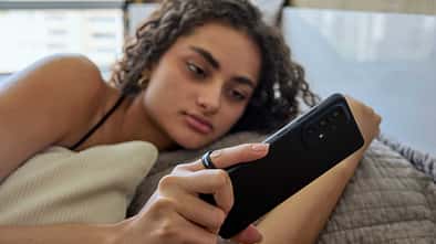 Frau liegt im Bett, blickt auf ihr Smartphone und trägt einen Smart Ring am Finger.