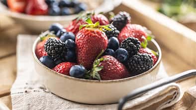 Ripe sweet different berries in a bowl on kitchen table.