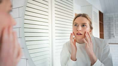 Skin analysis in mirror. Focused woman examines her face for signs of aging and wrinkles in bathroom