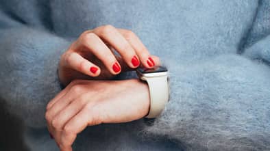 Hände mit rotlackierten Fingernägeln tippen auf Smartwatch