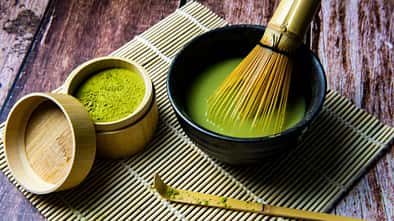 Matcha-Pulver und Matcha-Tee in einer Schale mit Bambusbesen auf einer Bambusmatte. Matcha-Pulver und Matcha-Tee in einer Schale mit Bambusbesen auf einer Bambusmatte.