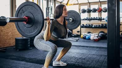 Junge Frau macht im Fitnessstudio einen Squat mit einer Langhantel auf den Schultern