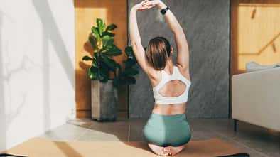 Junge Frau dehnt sich auf einer Yogamatte, indem sie ihre Arme nach oben ausstreckt.