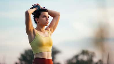 Junge Frau steht mit den Händen über dem Kopf zusammengenommen in der Natur 