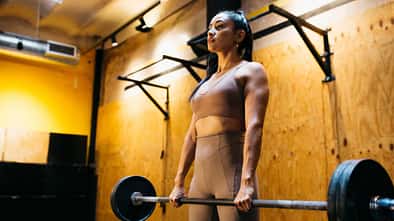 Eine junge Frau hebt im Fitnessstudio eine Langhantel