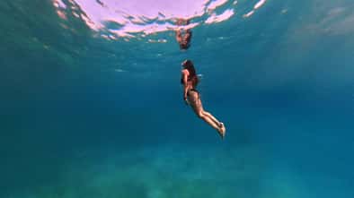 Unterwasseraufnahme einer Frau die elegant taucht und zur Wasseroberfläche hinaufblickt Unterwasseraufnahme einer Frau die elegant taucht und zur Wasseroberfläche hinaufblickt