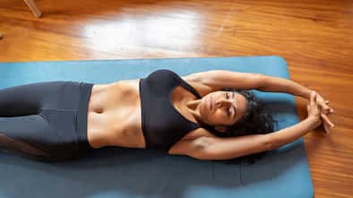 Eine Frau liegt mit geschlossenen Augen auf einer Yogamatte und macht hypopressive Bauchmuskelübungen