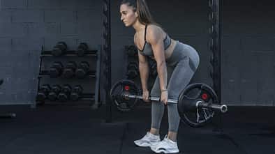 Sportliche Frau führt im Fitnessstudio eine Good Morning Übung mit einer Langhantel aus
