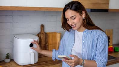 Eine Frau kocht mit dem Airfryer und schaut auf ihr Smartphone
