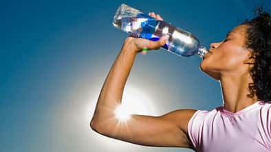 Eine Frau trinkt aus einer Plastikflasche, während im Hintergrund die Sonne scheint