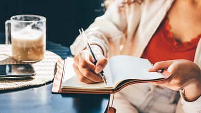 Eine Frau sitzt in einem Cafe an einem Tisch und schreibt in ihr Journal