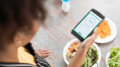 Frau checkt während dem Essen ihre Intervallfasten-App auf dem Smartphone