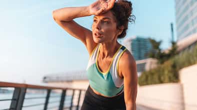 Frau in Fitnesskleidung hält sich während ihres Outdoor-Workouts in der Sonne die Hand an die Stirn