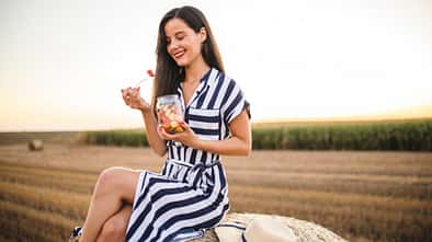 Frau isst Obst und sitzt auf einem Heuballen auf dem Feld Frau isst Obst und sitzt auf einem Heuballen auf dem Feld