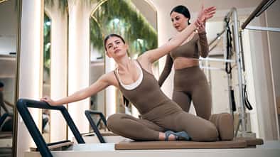 Eine Pilates-Trainerin unterstützt eine Frau beim Pilates-Training auf einer Reformer-Maschine