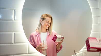 Frau mit einer Packung OMNi-BiOTiC® WOMAN und einem Glas in der Hand liest, was auf der Packung steht