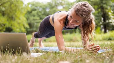 Frau macht im Park ein Workout mit einem Youtube-Video über ihren Laptop 