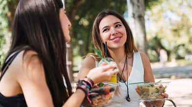Zwei junge Frauen sitzen im Park und essen Salat Zwei junge Frauen sitzen im Park und essen Salat
