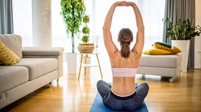 Eine Frau von hinten, wie sie auf einer Yogamatte Übungen für den Rücken praktiziert
