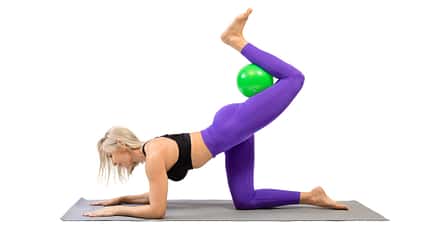 Beinkicks, Pilates-Ball Frau macht Beinkicks im Dreifüßlerstand mit Pilates-Ball in die Kniekehle geklemmt
