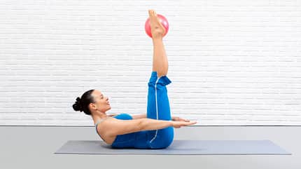 100, hundred, Crunch, Pilates Frau macht Crunches mit nach oben gestreckten Beinen. Sie hat einen Pilates-Ball zwischen die Füße geklemmt