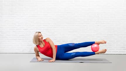 Seitheben, Pilates-Ball Frau liegt auf der Seite und hebt die Beine in die Luft, während sie einen Pilates-Ball zwischen die Füße klemmt