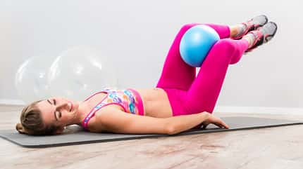 Pendeln, Pilates-Ball Frau in Rückenlage klemmt Ball zwischen die Knie und pendelt mit angezogenen Beinen von rechts nach links.