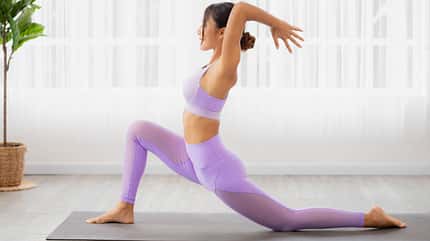 Weiße, asiatische Frau mit dunklen Haaren führt auf einer Matte eine Yoga-Übung aus Weiße, asiatische Frau mit dunklen Haaren führt auf einer Matte eine Yoga-Übung aus