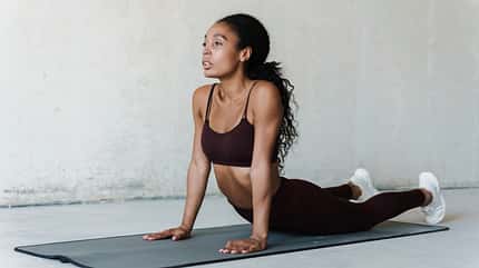 Eine Frau führt auf einer Matte eine Yoga-Übung durch Eine Frau führt auf einer Matte eine Yoga-Übung durch