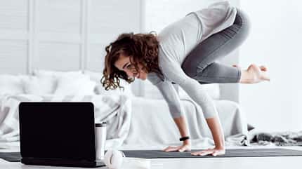 Eine Frau führt vor einem Laptop eine Yoga-Übung aus Eine Frau führt vor einem Laptop eine Yoga-Übung aus