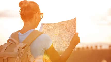 Eine Frau steht entgegen der Sonne mit einer Karte in der Hand in der Natur
