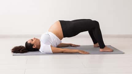 Beckenheben Frau mit Babybauch macht die Übungen Beckenheben auf der Matte.