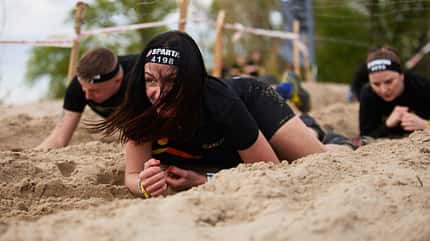 Crawling Frauen kriechen bei einem Sportwettkampf durch Sand.