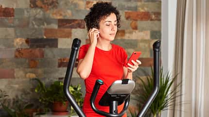 smartphone,bicycle,headphones,young adult,one person,red,music,f Woman,Exercising,On,Elliptical,Cross,Trainer,At,Home,Wearing,Wireless