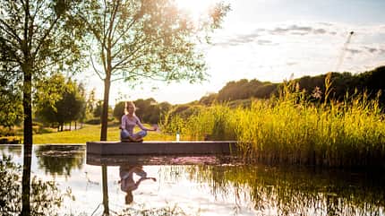 Eine Frau praktiziert Yoga-Übung an einem See in der Sonne Eine Frau praktiziert Yoga-Übung an einem See in der Sonne