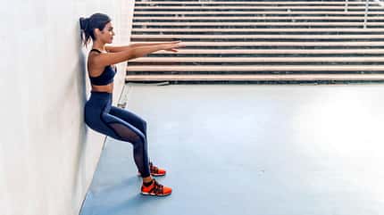 Frau in Sportkleidung praktiziert Wandsitzen Frau in Sportkleidung praktiziert Wandsitzen