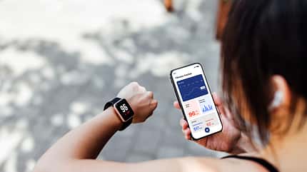 Young Woman Using Fitness Tracker App On Smart Watch And Smartphone