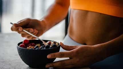 Frau bereitet Müsli in einer Schale zu in orangenem Sport Bh Frau bereitet Müsli in einer Schale zu in orangenem Sport Bh