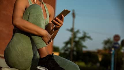 Junge Frau sitzt mit angewinkeltem Bein in Sportkleidung und hört Musik Junge Frau sitzt mit angewinkeltem Bein in Sportkleidung und hört Musik