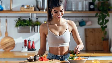Eine trainierte Frau steht in der Küche und bereitet eine Bowl zu
