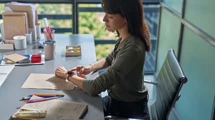 Eine Frau sitzt am Schreibtisch und bedient ihre Smartwatch Eine Frau sitzt am Schreibtisch und bedient ihre Smartwatch