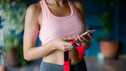 Frau im Fitnessstudio hält ihren Fitness-Tracker und richten Sie die App auf ihrem Handy Frau im Fitnessstudio hält ihren Fitness-Tracker und richten Sie die App auf ihrem Handy