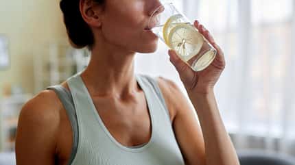 Sportliche Frau trinkt ein Glas Wasser mit Zitrone Sportliche Frau trinkt ein Glas Wasser mit Zitrone
