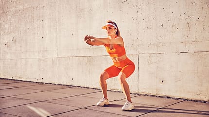 Athletic,Adult,Woman,Doing,Squat,Exercise,Outdoors,Against,Concrete,Wall